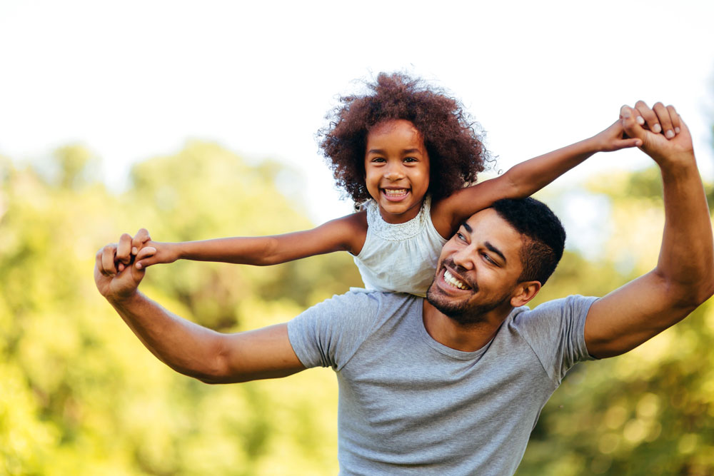 man holds hands of little girl riding on his back