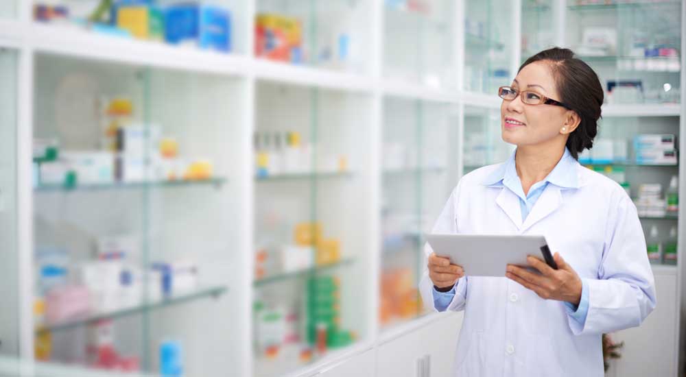 Woman in white coat looks at shelves of prescription pill bottles 