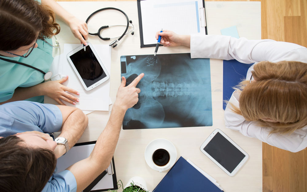 Overhead of three people looking at x ray of spine
