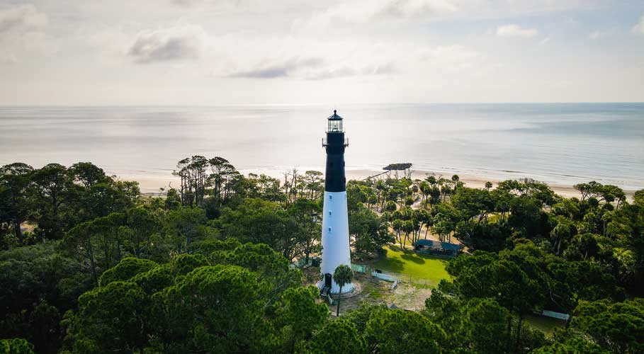 Lighthouse surrounded by trees with ocean and beach in background
