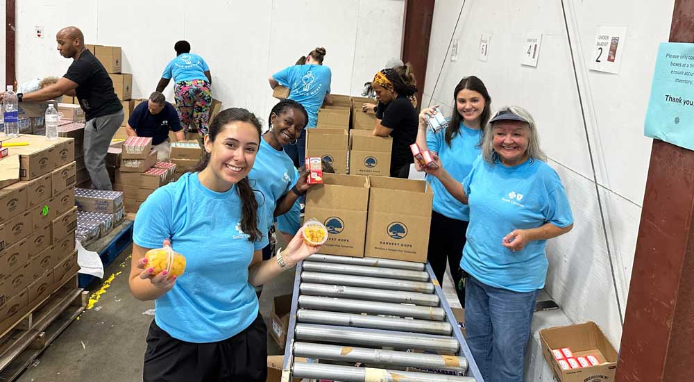 Group of employees wearing blue shirts with boxes of food and food items in warehouse 